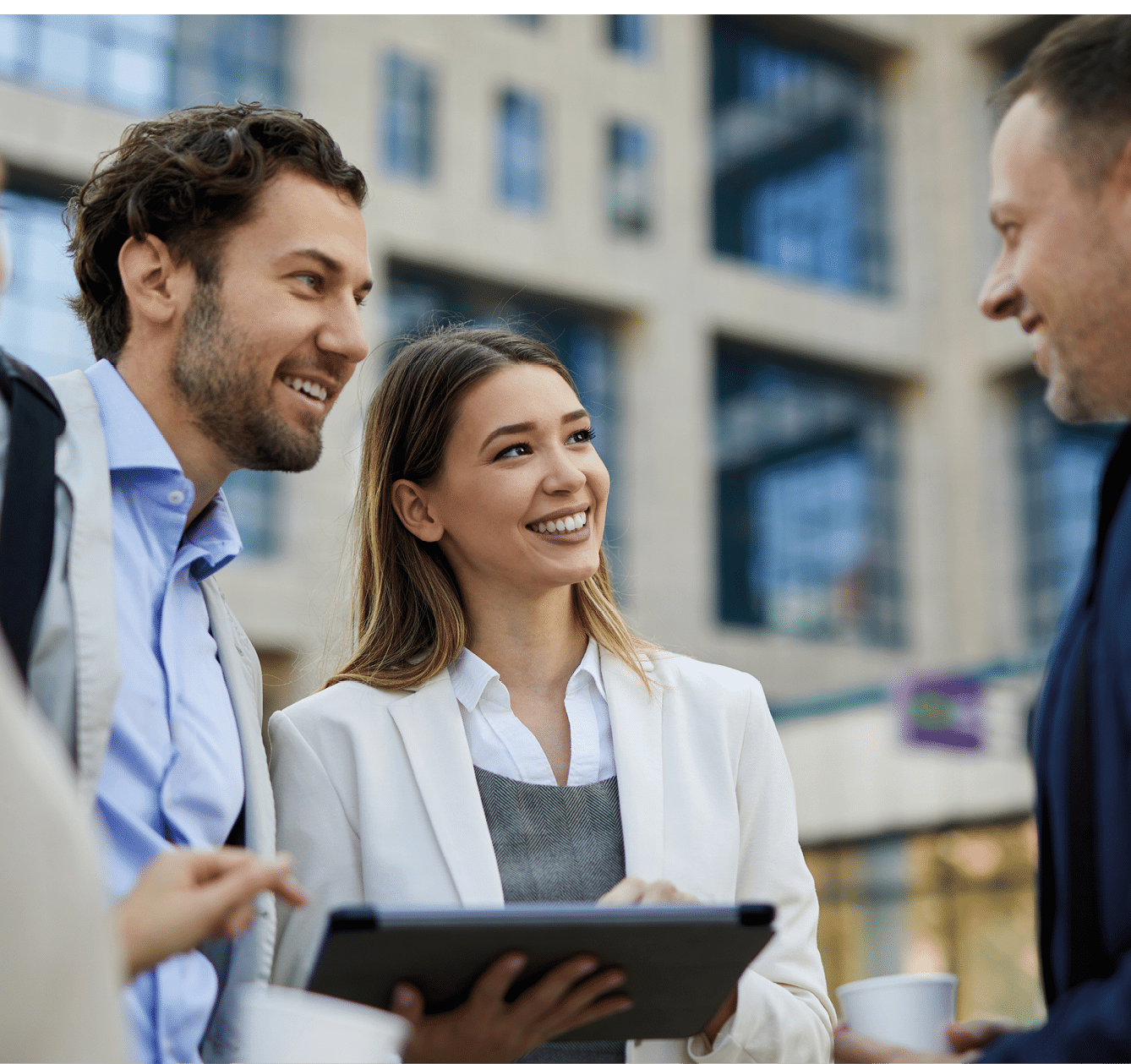 Two adults dressed in business attire are holding and looking at a tablet while standing outdoors near a building. Beskrivelse genereret af AI