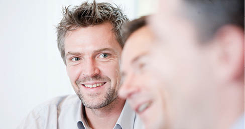 A close-up of a person smiling with visible facial hair and teeth. Beskrivelse genereret af AI