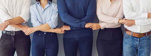 Five adults stand side by side with their arms linked, wearing casual and business casual clothing against a plain background. Beskrivelse genereret af AI
